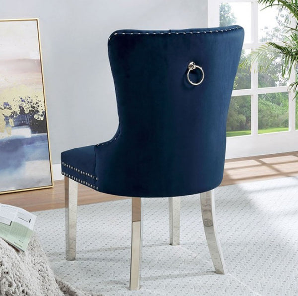 Noonwit Chrome Blue Flannelette Fabric Chair (2/PK) A high-back dining chair upholstered in dark navy blue velvet with silver nailhead trim and a silver ring pull on the backrest, shown in a bright room with a window and framed artwork.