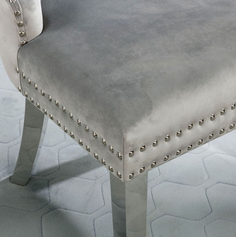 Noonwit Chrome Silver Flannelette Fabric Chair A high-back dining chair upholstered in light gray tufted velvet with silver nailhead trim and slim metallic legs, shown in a styled room setting with a gray wall, curtains, and a small plant.
