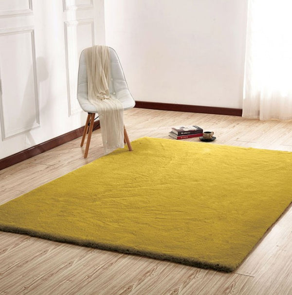 Patricia Power Loomed Modern Area Rug Yellow rug on a wooden floor with a white chair and books in the background.