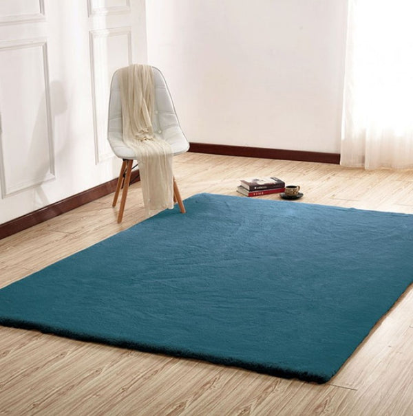 Patricia Power Loomed Modern Teal Area Rug Blue rug on a wooden floor with a white chair and books in the background.