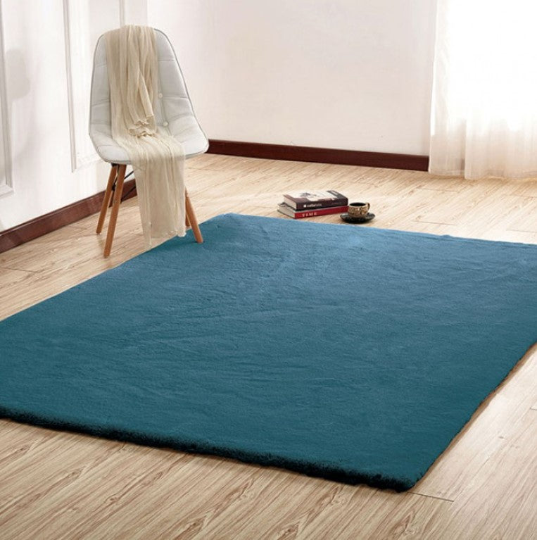 Patricia Power Loomed Modern Teal Area Rug Blue rug on a wooden floor with a white chair and books in the background.