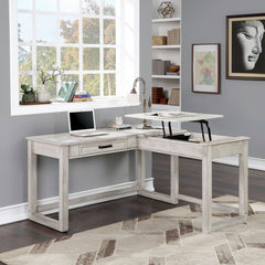 Prigala Antique White L-Shaped Corner Desk with USB Power Outlet An L-shaped corner desk in a distressed white wood finish, styled in a home office setting with a laptop, lamp, and adjustable desktop stand, set against a gray wall and dark wood floor.