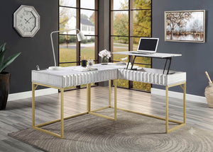 Primberg Antique White Two Tone Corner Desk An L-shaped computer desk with a white ribbed upholstered top and gold metal legs, shown in a modern home office setting with a standing lamp, laptop, and window view.