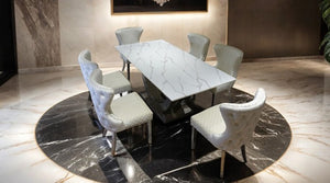 Primenova Horseshoe Shaped Sintered Stone Chrome White Dining Table A modern dining set featuring a rectangular white marble table with gray veining and six upholstered dining chairs in a luxurious marble-floored room.
