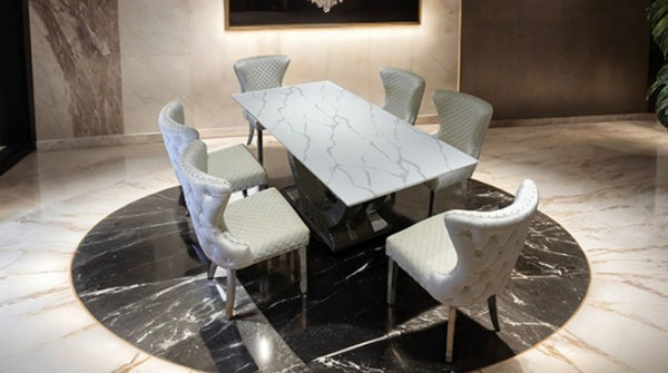 Primenova Horseshoe Shaped Sintered Stone Chrome White Dining Table A modern dining set featuring a rectangular white marble table with gray veining and six upholstered dining chairs in a luxurious marble-floored room.