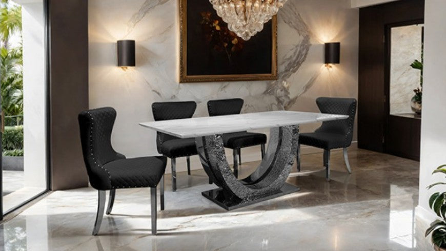 Primenova Horseshoe Shaped Sintered Stone Chrome White Dining Table A modern dining room set featuring a rectangular white marble-top table with a sculptural dark gray stone base, surrounded by four black upholstered dining chairs with silver metal legs, set in a luxury interior with marble floors and walls.