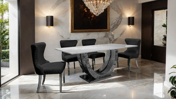Primenova Horseshoe Shaped Sintered Stone Chrome White Dining Table A modern dining room set featuring a rectangular white marble-top table with a sculptural dark gray stone base, surrounded by four black upholstered dining chairs with silver metal legs, set in a luxury interior with marble floors and walls.