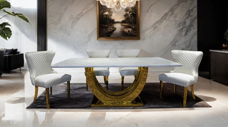 Primenova Upholstered Gold White Dining Chair A white quilted upholstered dining chair with gold-toned metal legs and nailhead trim, shown in a bright studio setting with a white wall and light wood floor.
