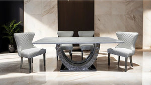 Primenova Upholstered Silver White Dining Chair A modern dining set featuring a rectangular white marble table with a sculptural curved metallic base and four matching light gray upholstered dining chairs, set in a luxury interior with marble walls and floors.