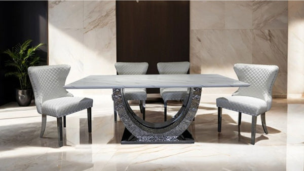 Primenova Upholstered Silver White Dining Chair A modern dining set featuring a rectangular white marble table with a sculptural curved metallic base and four matching light gray upholstered dining chairs, set in a luxury interior with marble walls and floors.