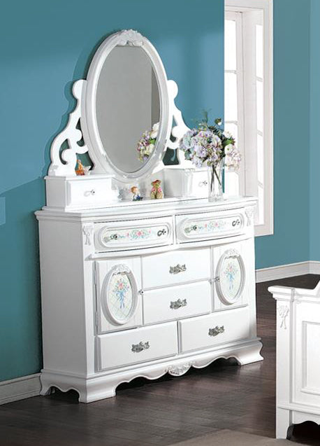 Primrose White Dresser with Floral Accent A white wooden dressing table with an attached oval mirror, ornate carved details, and multiple drawers, styled in a bedroom with a blue wall and dark wood floor.