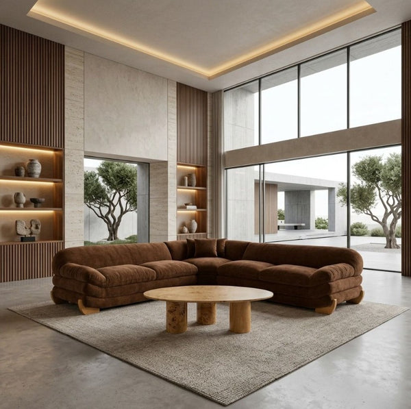 Prinkett Modular Corner Brown Fabric Sectional Sofa A modern sectional sofa in rich brown upholstery sits on a large light beige rug in a minimalist, high-ceilinged living room with wood slat walls, built-in shelves, and large windows overlooking trees and a patio.