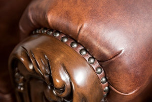 Prisya Traditional Leatherette Rolled Arm Sofa Close-up of a brown leather armchair with decorative nailhead trim