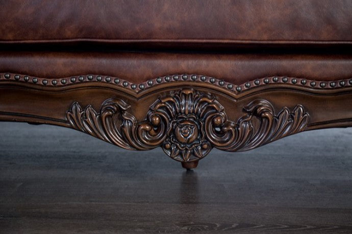 Prisya Traditional Leatherette Rolled Arm Chair Decorative brown leather sofa with intricate carvings in a room.