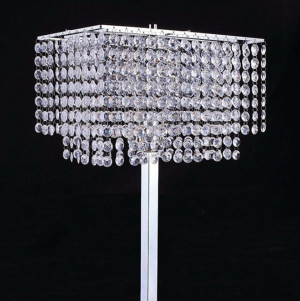 Remma Hanging Crystal Table Lamp A rectangular silver-toned chandelier-style table lamp covered in cascading clear crystal droplets, shown on a white stand against a black background.