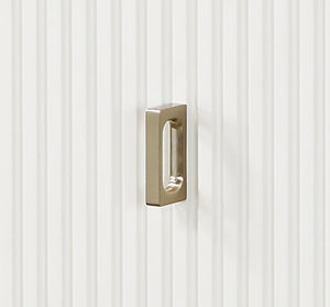Serania Two Tone Chest A modern rectangular pull handle with a rounded rectangular bar and a central oval cutout, finished in brushed gold metal, mounted on a white vertically ribbed surface.