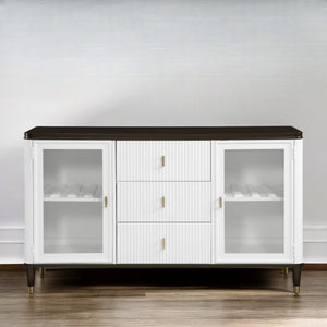 Serania Two Tone Dining Server A modern white sideboard cabinet with a dark brown top, glass-front doors on both sides, and three ribbed center drawers with small gold handles, shown against a light gray wall and wood floor.