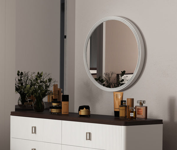 Serania Two Tone Wall Mirror Round mirror on a wall above a dresser with various bottles and a plant.