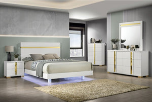 A modern bedroom furniture set featuring a white bed frame with gold accents, a matching nightstand, dresser, and tall storage cabinet, styled in a contemporary room with gray walls and wood flooring.
