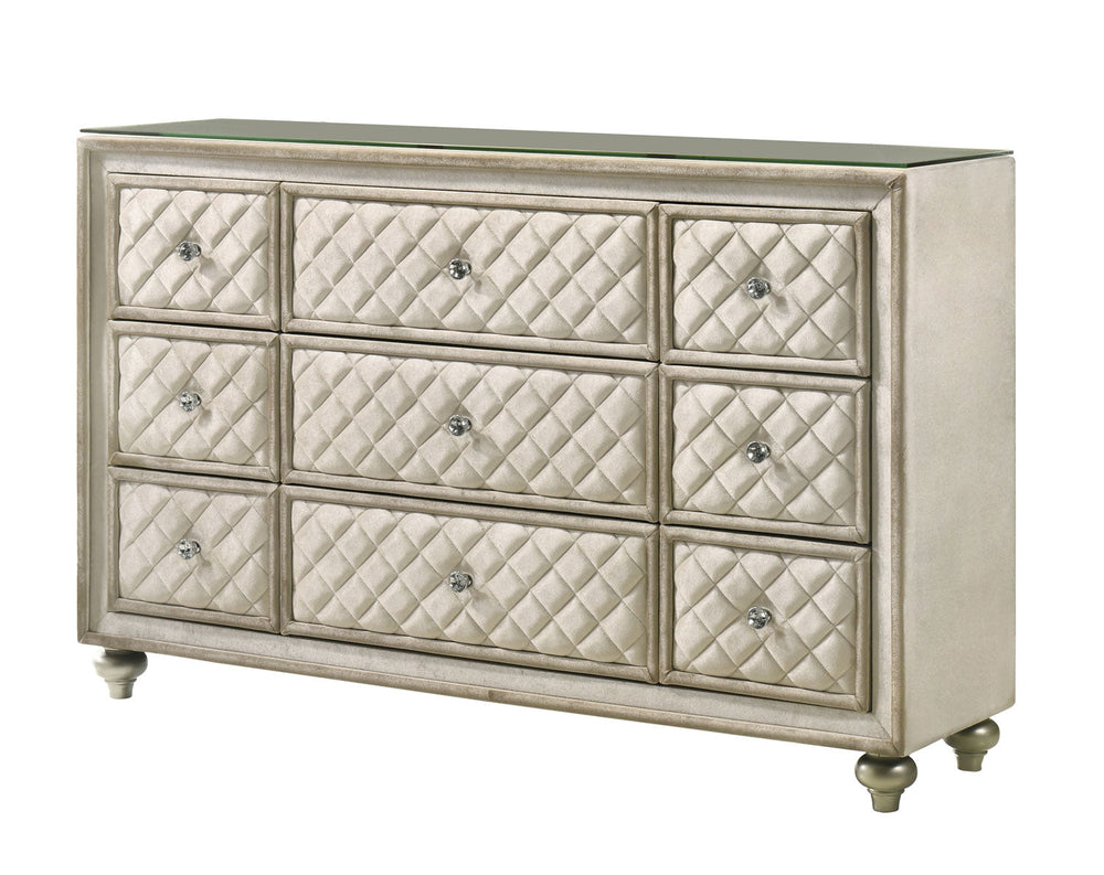 Sonya Beige Velvet Upholstered Traditional Style Dresser A nine-drawer dresser with quilted drawers and a matching arched mirror, both in a champagne gold and beige finish, set against a neutral paneled wall with sheer curtains.
