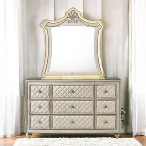Sonya Beige Velvet Upholstered Traditional Style Dresser A nine-drawer dresser with quilted drawers and a matching arched mirror, both in a champagne gold and beige finish, set against a neutral paneled wall with sheer curtains.