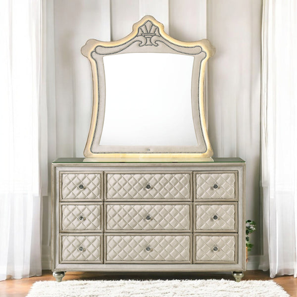 Sonya Beige Velvet Upholstered Traditional Style Dresser A nine-drawer dresser with quilted drawers and a matching arched mirror, both in a champagne gold and beige finish, set against a neutral paneled wall with sheer curtains.