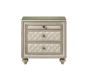 Sonya Beige Velvet Upholstered Traditional Style Nightstand A three-drawer nightstand with a distressed beige and silver finish, featuring quilted cream leatherette drawer fronts and a clear glass top, set against a plain white background.