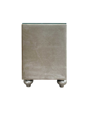 Sonya Beige Velvet Upholstered Traditional Style Nightstand A modern rectangular side table upholstered in a textured taupe fabric, featuring a clear glass top and two metallic silver ball feet, shown against a plain white background.
