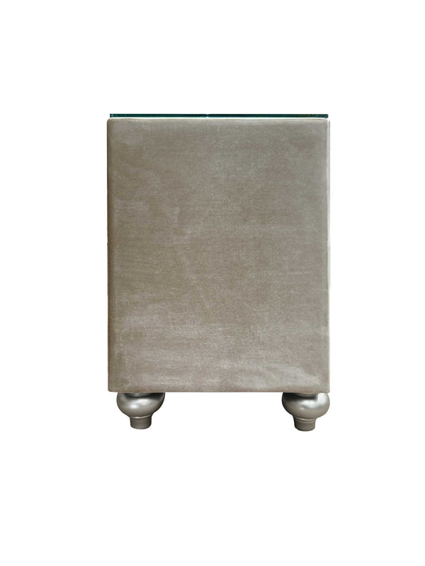 Sonya Beige Velvet Upholstered Traditional Style Nightstand A modern rectangular side table upholstered in a textured taupe fabric, featuring a clear glass top and two metallic silver ball feet, shown against a plain white background.