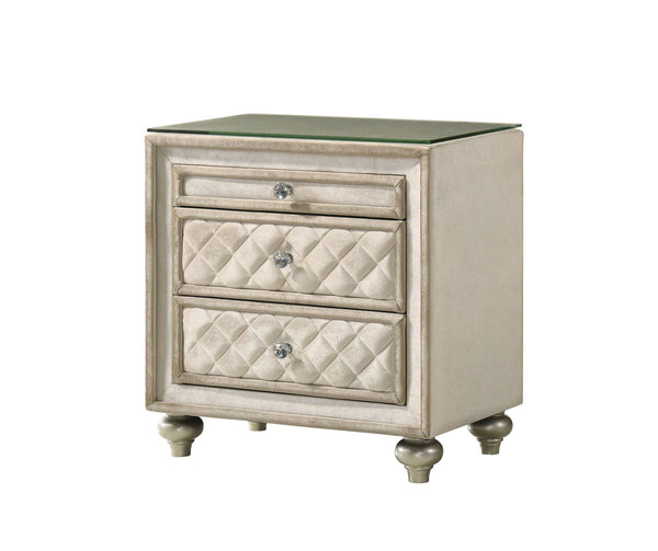 Sonya Beige Velvet Upholstered Traditional Style Nightstand A three-drawer nightstand with a distressed cream and silver finish, featuring quilted diamond-patterned drawer fronts, round silver knobs, and a clear glass top, shown on a plain white background.