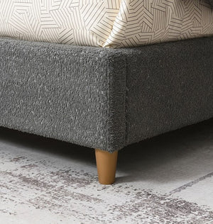Stivan Bed Fully Upholstered Gray Boucle Fabric Gray upholstered bed with wooden legs on a textured gray floor