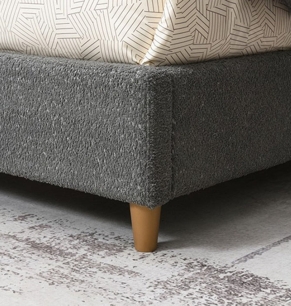 Stivan Bed Fully Upholstered Gray Boucle Fabric Gray upholstered bed with wooden legs on a textured gray floor