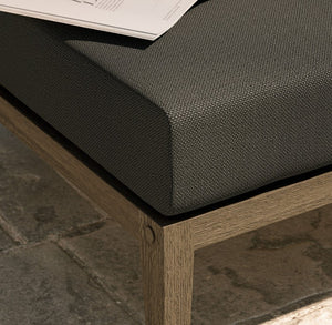 Sunshore Flint Gray Outdoor Ottoman Dark cushioned bench with wooden frame on a stone pavement