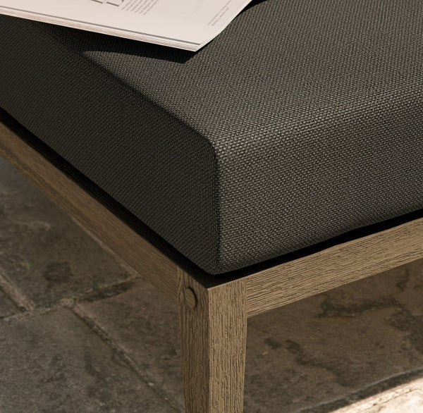 Sunshore Flint Gray Outdoor Ottoman Dark cushioned bench with wooden frame on a stone pavement