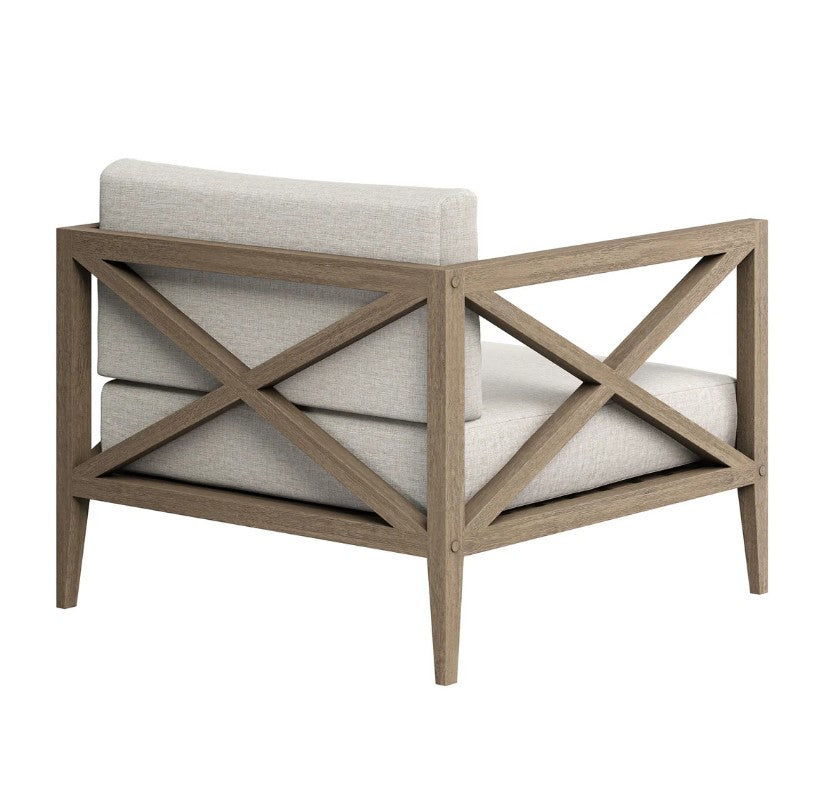 Sunshore Pebble Outdoor Armchair Outdoor chair with wooden frame and beige cushions, featuring a decorative pillow, on a stone patio.