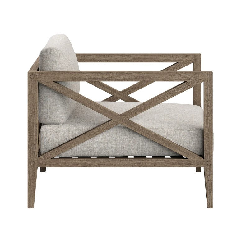 Sunshore Pebble Outdoor Armchair Outdoor chair with wooden frame and beige cushions, featuring a decorative pillow, on a stone patio.