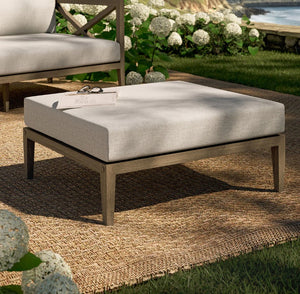 Sunshore Pebble Outdoor Ottoman Outdoor ottoman with cushion on a patio with hydrangeas and ocean view