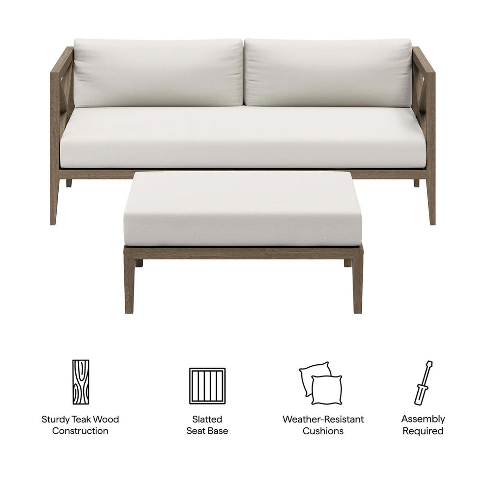 Sunshore Weathered Gray Loveseat and Ottoman Outdoor Set Outdoor patio set with sofa and ottoman on a stone patio, surrounded by flowers and a stone wall.