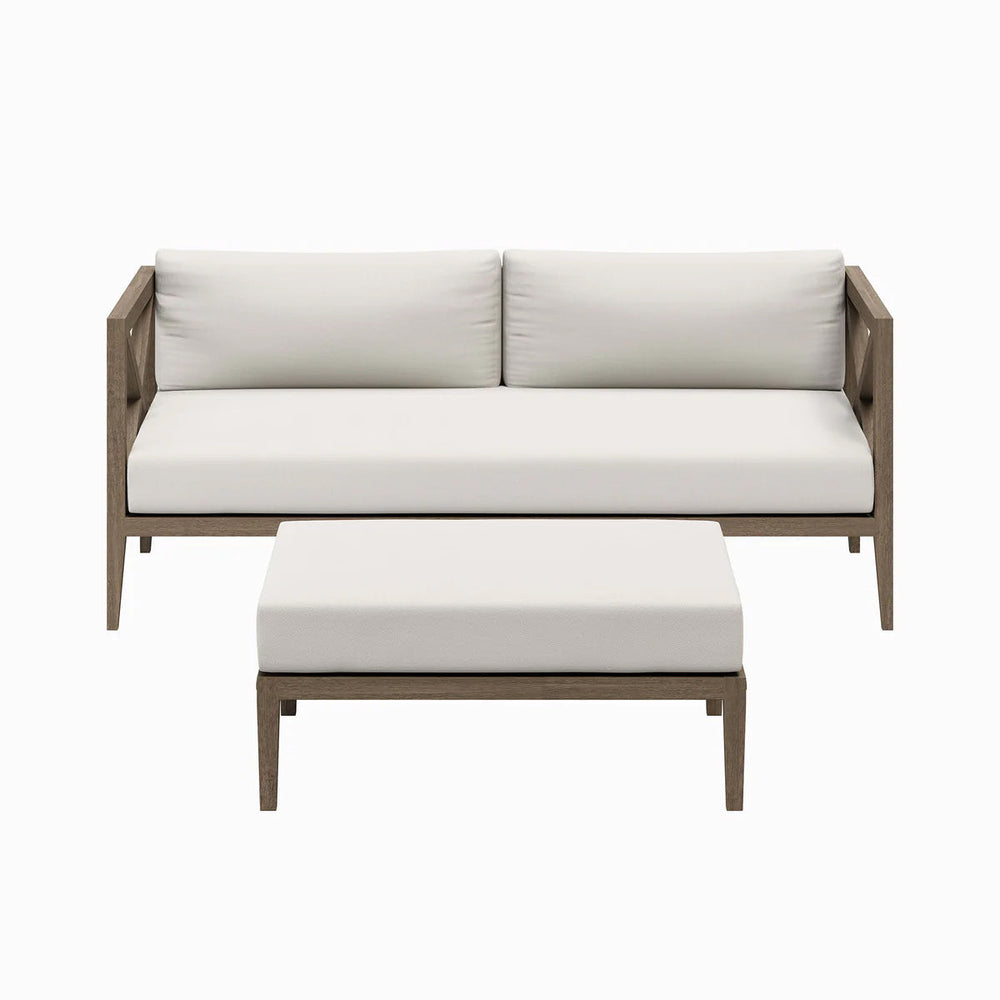 Sunshore Weathered Gray Loveseat and Ottoman Outdoor Set Outdoor patio set with sofa and ottoman on a stone patio, surrounded by flowers and a stone wall.