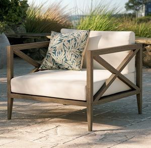 Sunshore Weathered Gray Outdoor Armchair Outdoor chair with white cushions and a patterned pillow on a stone patio.