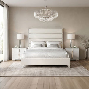 Sysko Glam Silver White Fully Upholstered Bed A modern bedroom featuring a white upholstered bed frame with a padded headboard and matching footboard, styled with white bedding, two matching white nightstands with silver lamps, a crystal chandelier, and a light gray rug on light wood flooring.