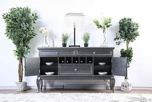 Gray sideboard with open doors displaying wine bottles, surrounded by decorative plants and vases on a white wall.