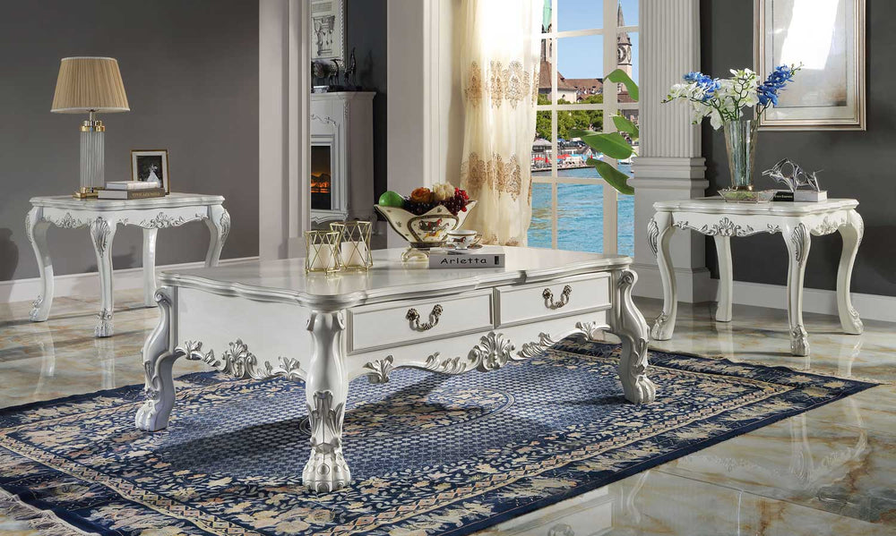 Traditional Style Coffee Table Bone White Dresden Collection An ornate white carved coffee table with two drawers and cabriole-style legs, shown in a staged living room setting with a blue patterned rug, side tables, and a window view.