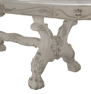 Traditional Style Dining Table Bone White Dresden Collection Close-up of an ornate carved table leg in a distressed off-white finish, showing intricate floral and scrollwork details against a plain white background.