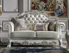 Traditional Style Loveseat Bone White Dresden Collection An ornate vintage-style loveseat sofa with carved silver-white wood, tufted button upholstery, and three decorative throw pillows, staged in a classic room with a large framed painting on the wall.