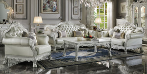 Traditional Style Sofa Bone White Dresden Collection An ornate white and silver carved sofa set with matching armchair, coffee table, and rug displayed in a luxurious decorated living room.