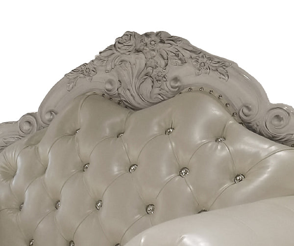 Traditional Style Sofa Bone White Dresden Collection Close-up of an ornate upholstered headboard with a carved floral crest, tufted button detailing, and small metallic nailhead accents on a white background.
