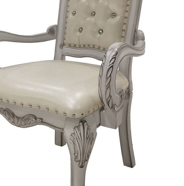 Traditional Style Dining Armchair Bone White Dresden Collection A close-up of a classic-style baroque dining chair with a light gray carved wooden frame and cream-colored tufted upholstery on the backrest and seat, accented with silver nailhead trim.