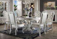 Traditional Style Round Dining Table Bone White Dresden Collection An ornate white carved dining room set featuring a round table and six matching high-back chairs with tufted upholstery, shown in a decorated dining room setting with a blue patterned rug and chandelier.