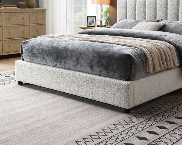 Traver Padded Vertical Channel Headboard Bed White Gray upholstered bed in a bedroom setting with a wooden dresser and lamp.